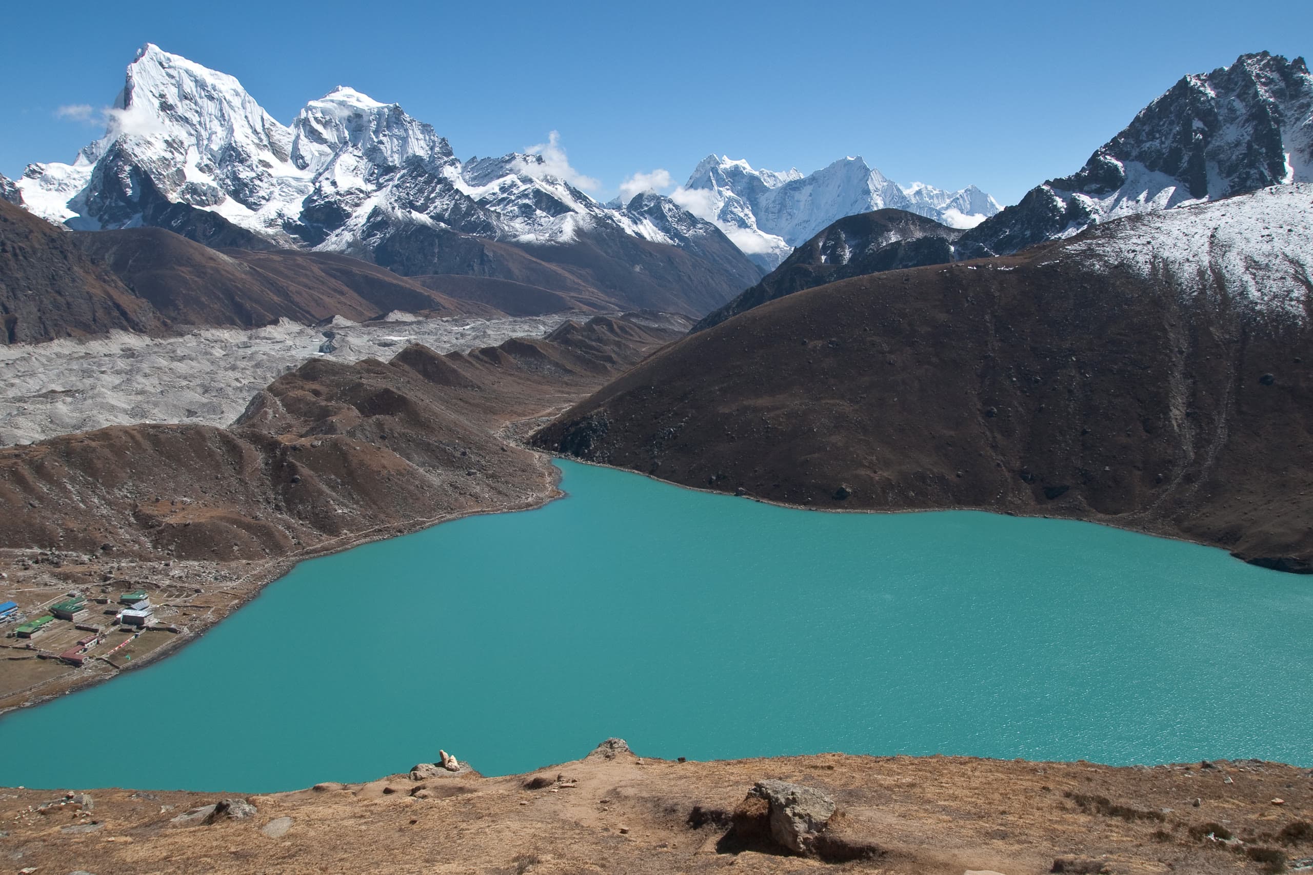 Vibrant sapphire turquoise glacial waters of Gokyo Lake surrounded by colossal Himalayan peaks